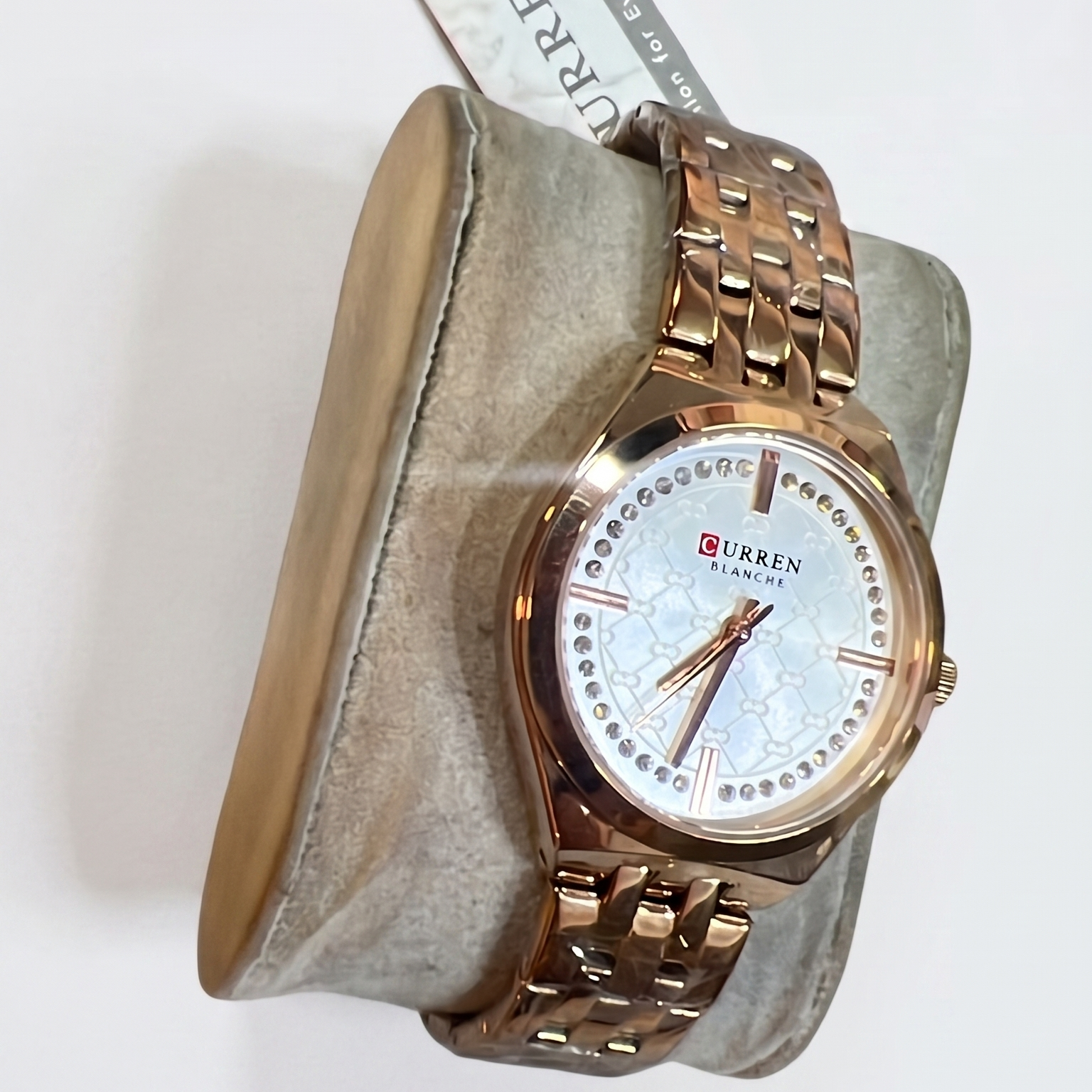 Rose gold watch with white face on a gray cushion, brand name visible